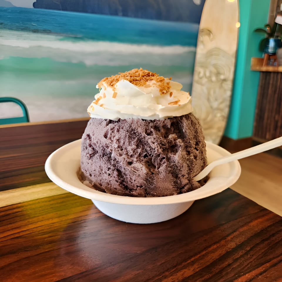 Hawaiian taro shave ice with whipped cream and toasted coconut flakes on a wooden table.